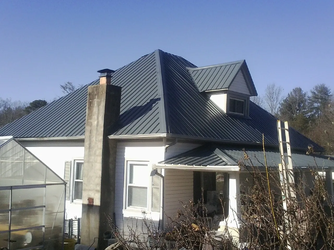 Dark blue standing seam metal roof on a white farmhouse with dormer — Slate & Tile Roof Repair by Roofing Brothers in Saratoga Springs