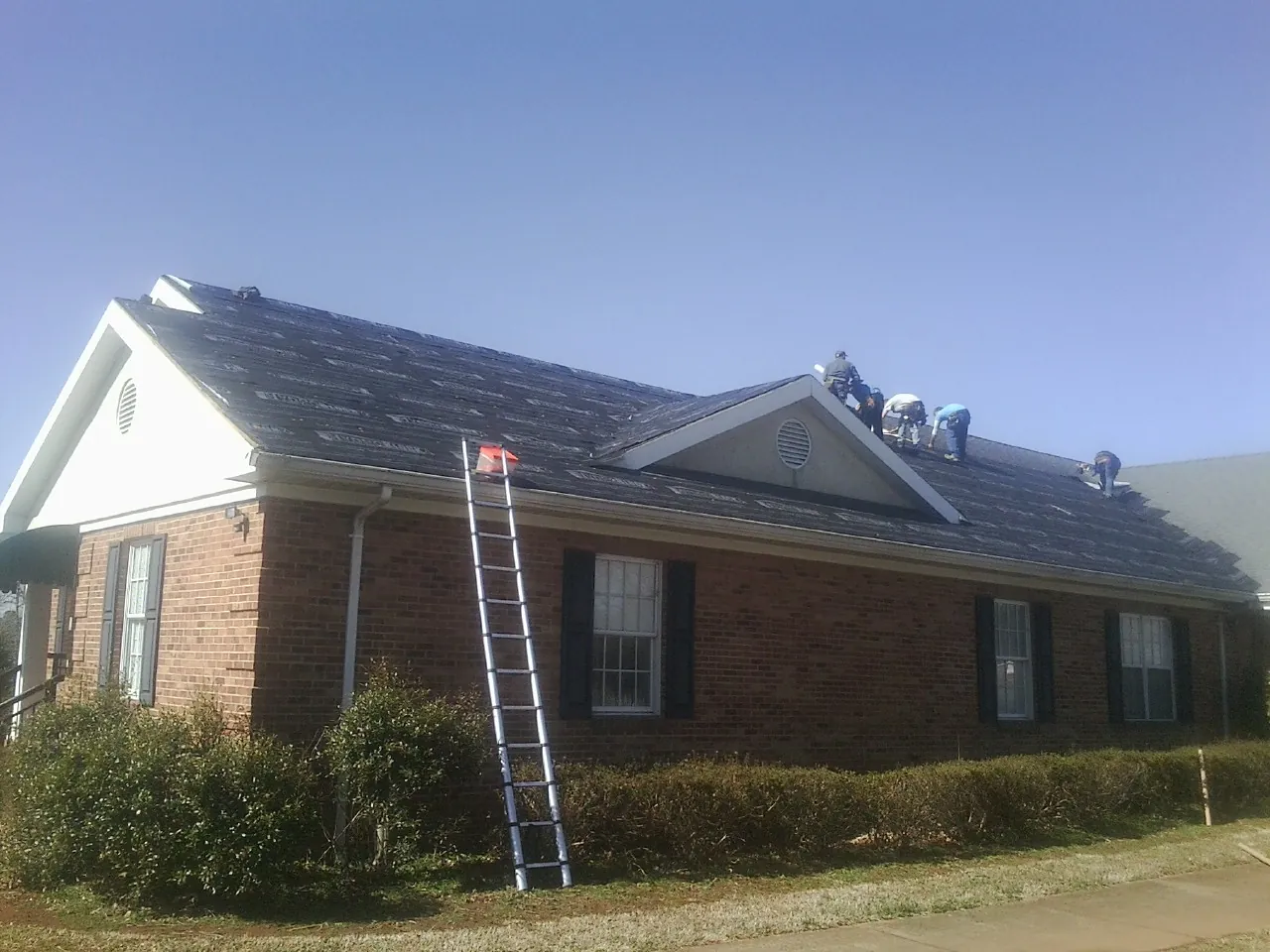 Crew tearing shingles off a brick ranch roof with a ladder set — Metal Roof Repair work by our crew in Saratoga Springs