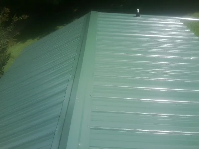 New green metal panels meeting at the ridge of a roof — Flat Roof Repair work by our crew in Saratoga Springs