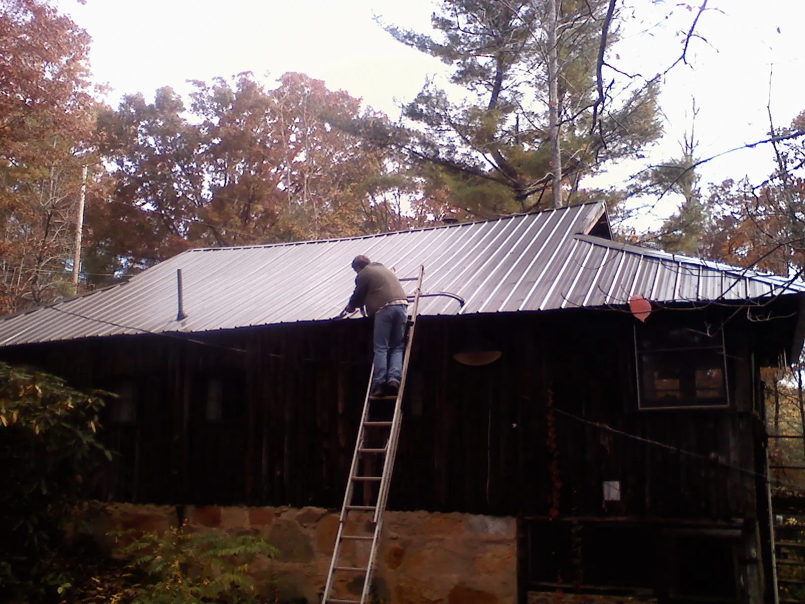 Roofer on a ladder working along the edge of a cabin metal roof in Saratoga Springs