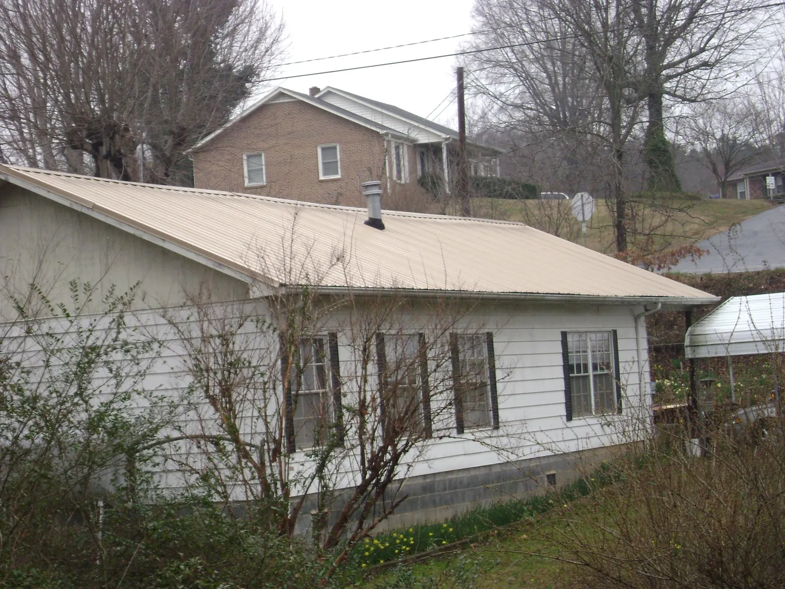 Tan metal roof on a white sided house set into a hillside — Commercial Roofing by Roofing Brothers in Saratoga Springs