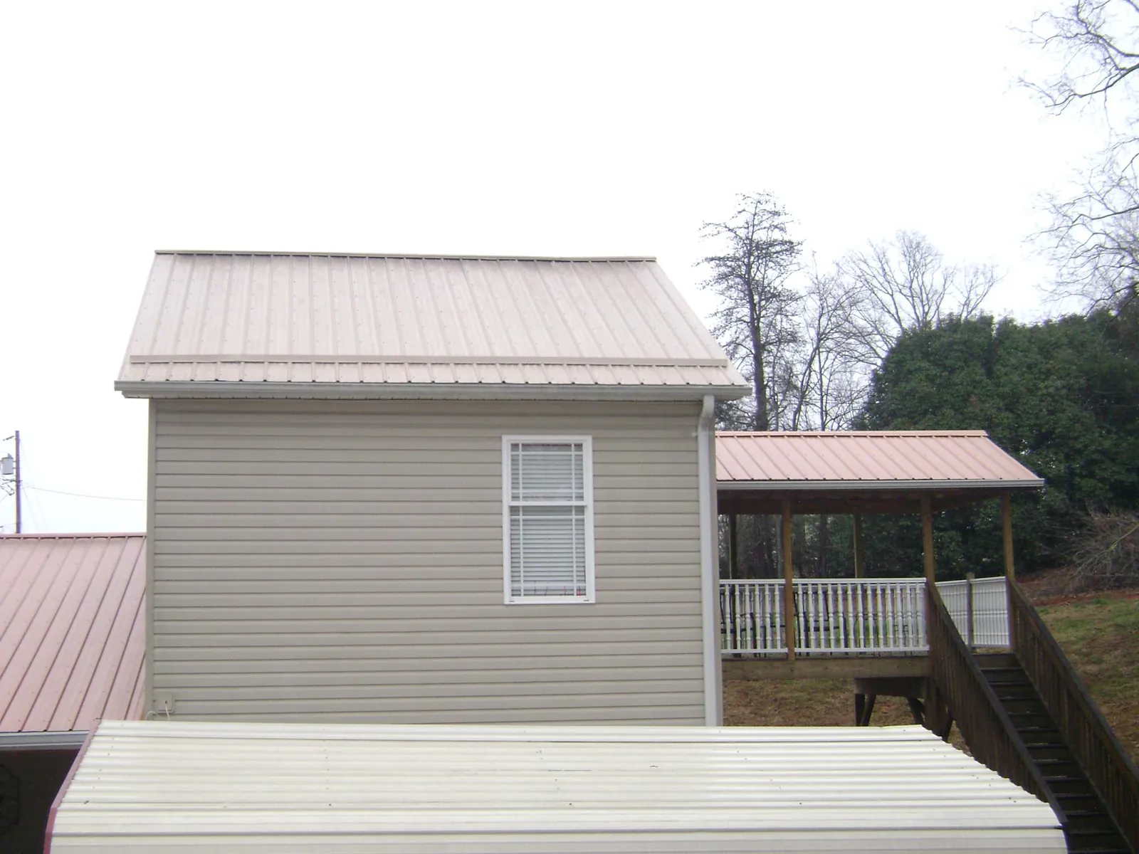 Tan metal roofs on a two story addition and attached porch, from a Roof Replacement job in Saratoga Springs
